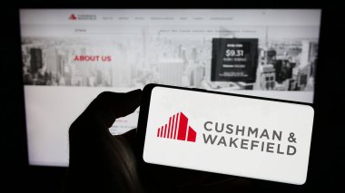 Stuttgart, Almanya - 07-15-2023: Emlak şirketi Cushman Wakefield plc 'nin logosunu taşıyan cep telefonu web sayfasının önünde duran kişi. Telefon ekranına odaklan.
