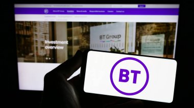 Stuttgart, Germany - 07-14-2023: Person holding smartphone with logo of British telecommunications company BT Group plc on screen in front of website. Focus on phone display. clipart