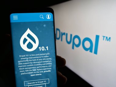 Stuttgart, Almanya - 07-13-2023: İçerik yönetim sistemi Drupal 'ın web sitesi olan cep telefonu logonun önünde ekranda. Telefon ekranının merkezine odaklan.
