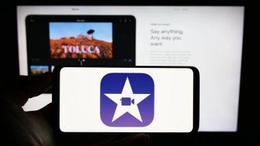 Stuttgart, Almanya - 07-12-2023: Web sayfası önünde ekranda video düzenleme yazılımı iMovie (Apple Inc.) logosu olan cep telefonu tutan kişi. Telefon ekranına odaklan.