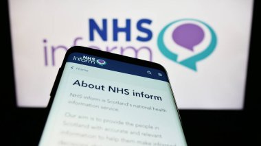 Stuttgart, Almanya - 07-12-2023: İskoç sağlık bilgi servisi NHS 'nin web sitesiyle birlikte cep telefonu logonun önünde ekranda yer alıyor. Telefon ekranının sol üst kısmına odaklan.