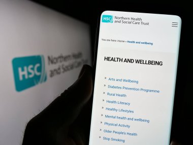 Stuttgart, Almanya - 07-12-2023: Kuzey İrlanda 'da Sağlık ve Sosyal Hizmetler (HSC) sitesinin logolu akıllı telefon sahibi kişi. Telefon ekranının merkezine odaklan.