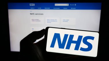 Stuttgart, Almanya - 07-12-2023: İngiliz Ulusal Sağlık Servisi 'nin (NHS) logosuna sahip cep telefonu web sayfası önünde ekranda. Telefon ekranına odaklan.