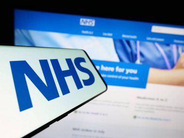 Stuttgart, Almanya - 07-12-2023: İnternet sitesinin önünde ekranda İngiliz Ulusal Sağlık Servisi (NHS) logosu bulunan cep telefonu. Telefon ekranının merkezine odaklan.