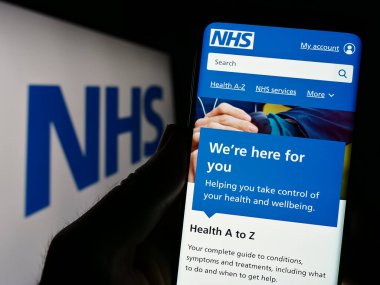 Stuttgart, Almanya - 07-12-2023: Logo önündeki ekranda İngiliz Ulusal Sağlık Servisi 'nin (NHS) web sayfası bulunan kişi. Telefon ekranının merkezine odaklan.