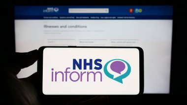 Stuttgart, Almanya - 07-12-2023: İskoç sağlık hizmetleri NHS logosuna sahip cep telefonu sahibi kişi web sayfası önünde ekranda yer alıyor. Telefon ekranına odaklan.