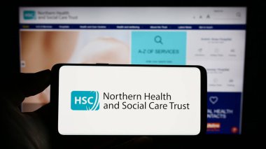 Stuttgart, Germany - 07-12-2023: Person holding cellphone with logo of Health and Social Care (HSC) in Northern Ireland on screen in front of webpage. Focus on phone display. clipart