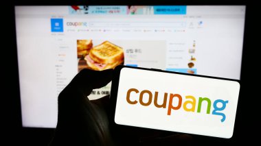 Stuttgart, Almanya - 07-11-2023: Koreli e-ticaret şirketi Coupang Inc. 'in logosunun bulunduğu cep telefonu sahibi kişi iş sayfasının önünde ekranda. Telefon ekranına odaklan.