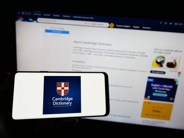 Stuttgart, Almanya - 07-11-2023: Cep telefonunda Cambridge Sözlüğü logosu olan kişi web sayfasının önünde ekranda. Telefon ekranına odaklan.
