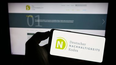 Stuttgart, Almanya - 07-11-2023: İnternet sayfası önünde üzerinde Deutscher Nachhaltigkeitskodex (DNK) logosu bulunan kişi. Telefon ekranına odaklan.