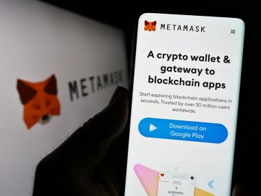 Stuttgart, Almanya - 07-11-2023: Cep telefonunda şifreli cüzdan yazılımı MetaMask web sayfası bulunan kişi logonun önünde ekranda. Telefon ekranının merkezine odaklan.