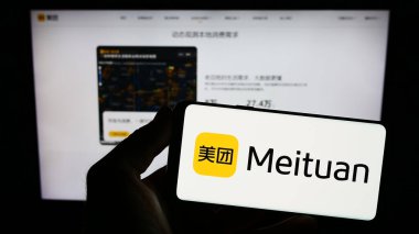 Stuttgart, Almanya - 07-11-2023: Çinli e-ticaret şirketi Meituan 'ın logosunu elinde tutan kişi web sitesinin önünde ekranda. Telefon ekranına odaklan.