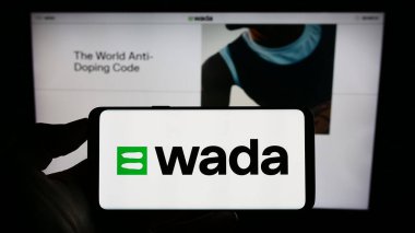 Stuttgart, Germany - 07-09-2023: Person holding mobile phone with logo of organization World Anti-Doping Agency (WADA) on screen in front of web page. Focus on phone display. clipart