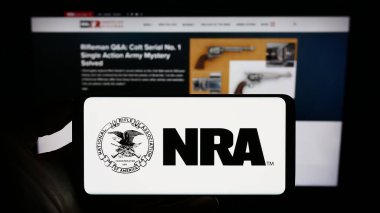 Stuttgart, Almanya - 07-09-2023: İnternet sayfası önünde üzerinde Ulusal Tüfek Birliği (NRA) logosu bulunan cep telefonu sahibi kişi. Telefon ekranına odaklan.