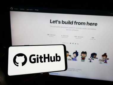 Stuttgart, Almanya - 07-09-2023: İnternet sayfasının önünde ekranda ABD 'li yazılım geliştirme şirketi GitHub Inc.' in logosuna sahip cep telefonu tutan kişi. Telefon ekranına odaklan.