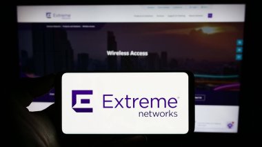 Stuttgart, Germany - 07-08-2023: Person holding cellphone with logo of US networking company Extreme Networks Inc. on screen in front of business webpage. Focus on phone display. clipart