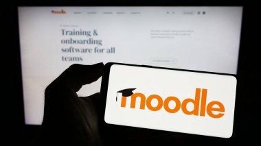 Stuttgart, Almanya - 07-08-2023: Web sayfası önünde ekranda Moodle öğrenme platformunun logosuna sahip cep telefonu tutan kişi. Telefon ekranına odaklan.