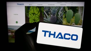 Stuttgart, Almanya - 07-08-2023: İnternet sayfası önünde Truong Hai Auto Corporation (THACO) şirketinin logosuyla cep telefonu tutan kişi. Telefon ekranına odaklan.