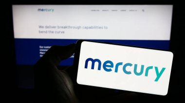 Stuttgart, Germany - 07-08-2023: Person holding cellphone with logo of US defense company Mercury Systems Inc. on screen in front of business webpage. Focus on phone display. clipart