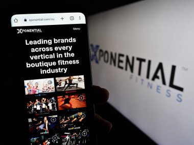 Stuttgart, Almanya - 07-08-2023: ABD 'li bayilik şirketi Xponential Fitness Inc.' in web sayfası ile cep telefonu tutan kişi logolu ekranda. Telefon ekranının merkezine odaklan.