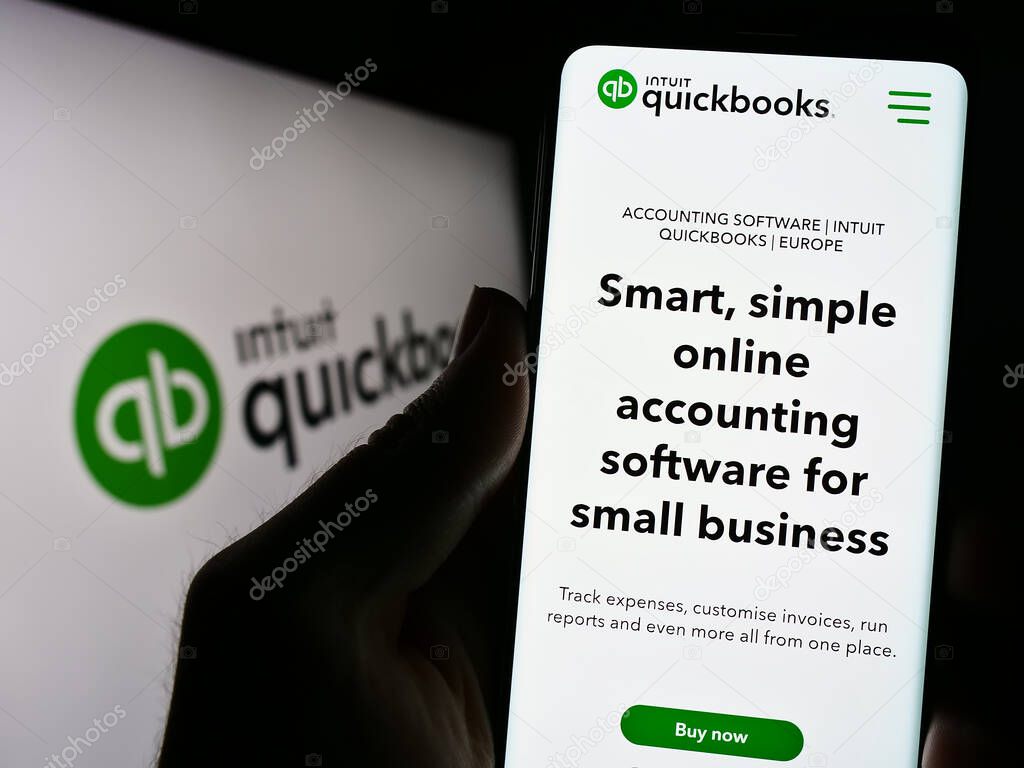 Stuttgart, Germany - 07-09-2023: Person holding cellphone with webpage of accounting software QuickBooks on screen in front of logo. Focus on center of phone display.