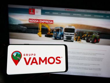 Stuttgart, Almanya - 07-06-2023: Brezilyalı kamyon kiralama şirketi Grupo Vamos 'un logosunu elinde tutan kişi web sitesinin önünde ekranda. Telefon ekranına odaklan.