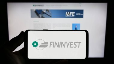 Stuttgart, Almanya - 07-06-2023: İtalyan holding şirketi Fininvest S.P.A. 'nın logosunu elinde tutan kişi web sitesinin önünde ekranda. Telefon ekranına odaklan.