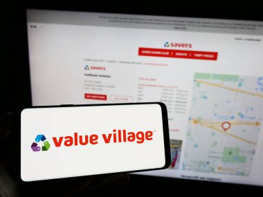 Stuttgart, Germany - 07-06-2023: Person holding mobile phone with logo of retail company Value Village (Savers) on screen in front of business web page. Focus on phone display. clipart