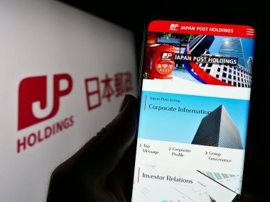 Stuttgart, Almanya - 07-04-2023: Japon şirketi Japan Post Holding Co. Ltd. nin internet sayfası ile cep telefonu tutan kişi logo ile ekranda. Telefon ekranının merkezine odaklan.