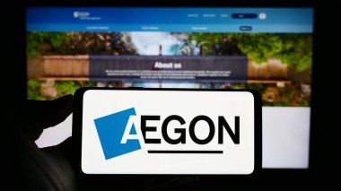 Stuttgart, Almanya - 07-04-2023: Hollandalı finans hizmetleri şirketi Aegon NV 'nin logosuyla cep telefonu sahibi kişi iş sayfası önünde ekranda. Telefon ekranına odaklan.