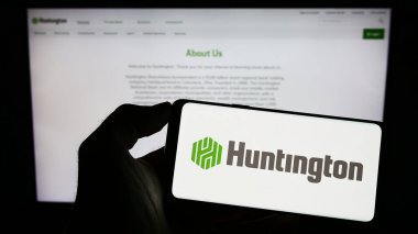 Stuttgart, Almanya - 07-02-2023: ABD 'li Huntington Bancshare Anonim Şirketi' nin logosunu elinde tutan kişi web sitesinin önünde ekranda. Telefon ekranına odaklan.