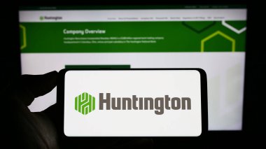 Stuttgart, Almanya - 07-02-2023: Web sayfası önünde ekranda Huntington Bancshare Anonim Şirketi 'nin logosuyla cep telefonu tutan kişi. Telefon ekranına odaklan.