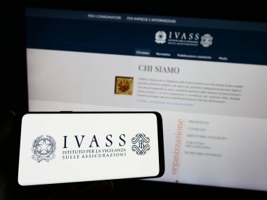 Stuttgart, Almanya - 07-02-2023: İtalyan sigorta denetleme yetkilisi IVASS logosuna sahip akıllı telefon sahibi kişi web sayfasının önünde ekranda. Telefon ekranına odaklan.