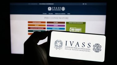 Stuttgart, Almanya - 07-02-2023: İtalyan sigorta denetleme yetkilisi IVASS logosuna sahip akıllı telefon sahibi kişi web sitesinin önünde ekranda. Telefon ekranına odaklan.