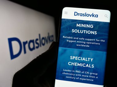 Stuttgart, Germany - 07-02-2023: Person holding cellphone with website of Czech chemical company Draslovka Holding a.s. on screen with logo. Focus on center of phone display. clipart