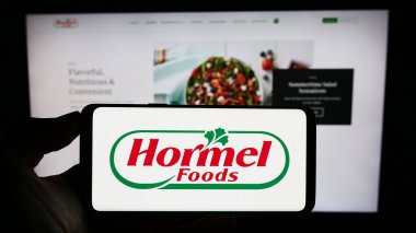 Stuttgart, Almanya - 07-02-2023: ABD 'li gıda şirketi Hormel Foods Corporation' ın logosunu elinde tutan kişi web sitesinin önünde ekranda. Telefon ekranına odaklan.