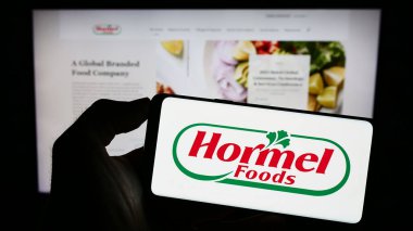 Stuttgart, Almanya - 07-02-2023: ABD 'li gıda şirketi Hormel Foods Corporation' ın logosuyla cep telefonu sahibi kişi iş sayfasının önünde ekranda. Telefon ekranına odaklan.