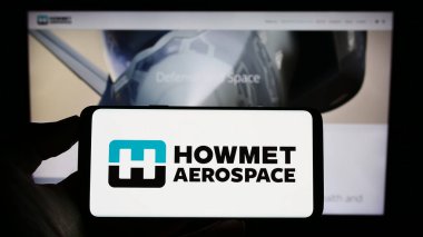 Stuttgart, Almanya - 07-02-2023: ABD 'li firma Howmet Aerospace Inc.' in logosuyla cep telefonu sahibi kişi iş sayfasının önünde ekranda. Telefon ekranına odaklan.