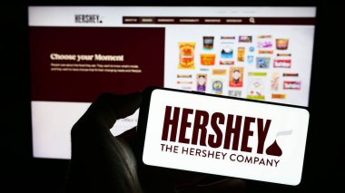 Stuttgart, Germany - 07-02-2023: Person holding cellphone with logo of US food business The Hershey Company on screen in front of business webpage. Focus on phone display. clipart