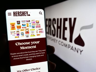 Stuttgart, Almanya - 07-02-2023: ABD gıda şirketinin web sayfası ile akıllı telefon tutan kişi The Hershey Company logonun önünde ekranda. Telefon ekranının merkezine odaklan.