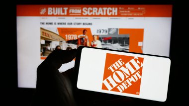 Stuttgart, Almanya - 07-02-2023: ABD 'li perakende şirketi The Home Depot Inc.' in logosuyla cep telefonu sahibi kişi iş sayfasının önünde ekranda. Telefon ekranına odaklan.