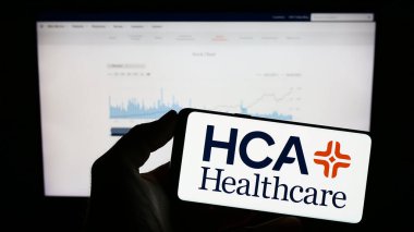 Stuttgart, Almanya - 07-02-2023: ABD 'li HCA Healthcare Inc. şirketinin logosuyla cep telefonu sahibi kişi iş sayfasının önünde ekranda. Telefon ekranına odaklan.