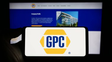 Stuttgart, Germany - 07-01-2023: Person holding smartphone with logo of US business Genuine Parts Company (GPC) on screen in front of website. Focus on phone display. clipart