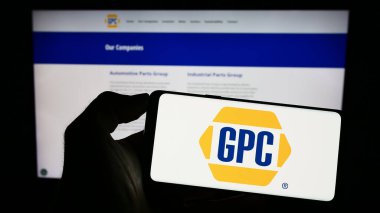 Stuttgart, Germany - 07-01-2023: Person holding cellphone with logo of US business Genuine Parts Company (GPC) on screen in front of business webpage. Focus on phone display. clipart