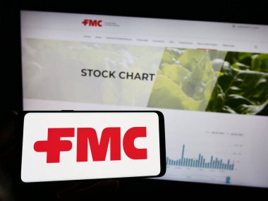 Stuttgart, Germany - 07-01-2023: Person holding mobile phone with logo of American chemical company FMC Corporation on screen in front of web page. Focus on phone display. clipart