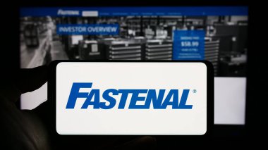 Stuttgart, Almanya - 07-01-2023: ABD 'li dağıtım şirketi Fastenal Company' nin logosunu elinde tutan kişi web sitesinin önünde ekranda. Telefon ekranına odaklan.