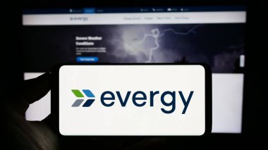 Stuttgart, Almanya - 07-01-2023: Amerikan hizmet şirketi Evergy Inc. 'in logosunu taşıyan cep telefonu sahibi kişi iş sayfasının önünde ekranda. Telefon ekranına odaklan.