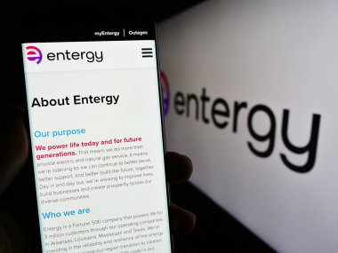 Stuttgart, Germany - 07-01-2023: Person holding cellphone with web page of US energy company Entergy Corporation on screen in front of logo. Focus on center of phone display. clipart