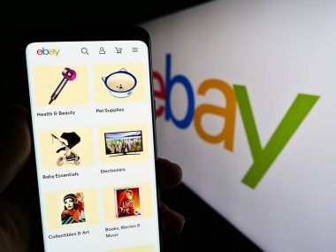 Stuttgart, Almanya - 07-01-2023: ABD e-ticaret şirketi eBay Inc. 'nin web sayfası ile akıllı telefonu olan kişi iş logosu önünde ekranda. Telefon ekranının merkezine odaklan.