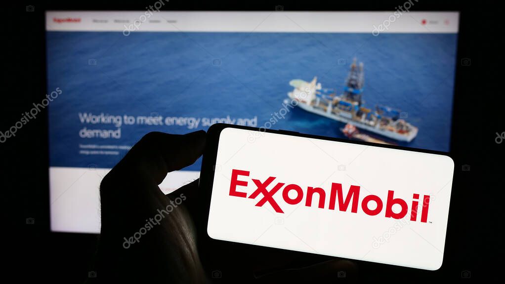 Stuttgart, Germany - 07-01-2023: Person holding cellphone with logo of American petroleum company Exxon Mobil Corporation on screen in front of webpage. Focus on phone display.